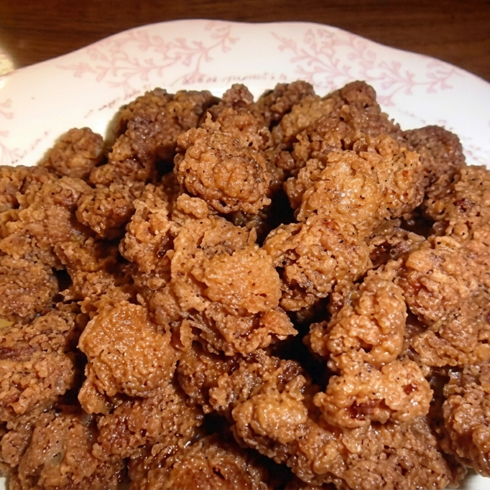 Plate piled with golden-brown crispy fried chicken pieces on a floral-rimmed dish atop a wooden table.
